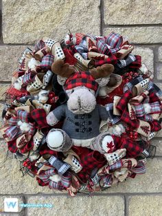 a wreath with a stuffed animal in the middle and plaid fabric around it, hanging on a brick wall