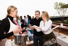 two women and one man are serving food on a rooftop deck at an outdoor event