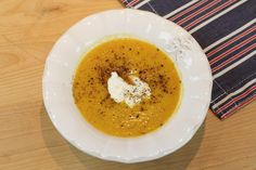 a white bowl filled with soup sitting on top of a wooden table next to a striped napkin