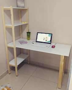 a laptop computer sitting on top of a white desk next to a wooden shelf with shelves