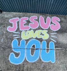 the words jesus loves you are painted on concrete with blue and pink spray paint over it