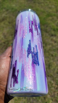 a hand holding a purple and blue flask with stars on the side, in front of grass