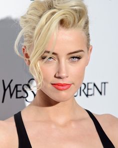 a woman with blonde hair and bright orange lipstick on her face, wearing a black dress