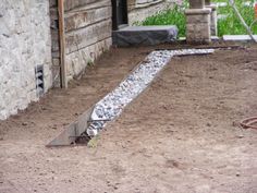 a bird is standing in the dirt next to a building with rocks and gravel on it