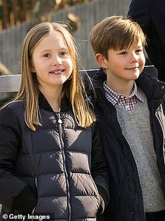 two young children standing next to each other in front of a wooden fence with an animal behind them