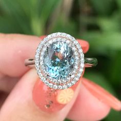 a woman's hand holding a ring with an oval blue topaz surrounded by diamonds