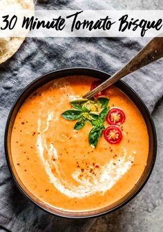 a bowl of tomato soup with basil and tomatoes on the side, next to bread