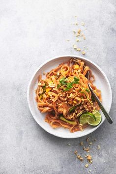 a white bowl filled with noodles and vegetables on top of a gray surface next to chopsticks