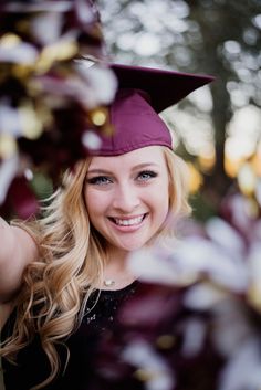 a woman wearing a purple graduation cap and gown posing for a photo in front of some trees