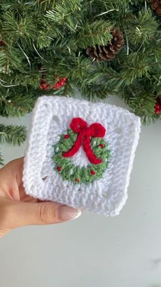 someone is holding up a crocheted christmas ornament in front of a tree