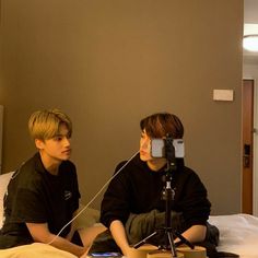 two boys are sitting on a bed and one boy is recording something with a camera