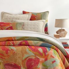 a bed with colorful comforter and pillows on it in a room next to a lamp