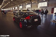 a black car parked in a garage with people walking around the area and onlookers looking at it