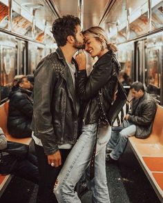 a man and woman standing on a subway train kissing each other's foreheads