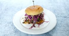 a white plate topped with a burger covered in coleslaw