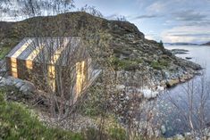 a small house sitting on top of a lush green hillside next to a body of water