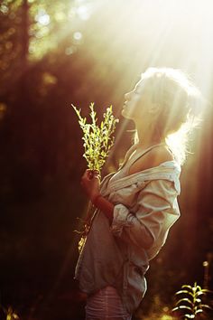 a woman holding a plant in her hands with the sun shining down on her face