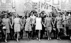 a group of women standing next to each other in front of a crowd holding signs