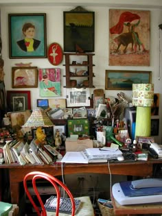 a cluttered desk with lots of art on the wall and pictures hanging above it