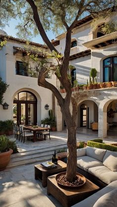 an outdoor living area with couches, tables and a tree in front of a house