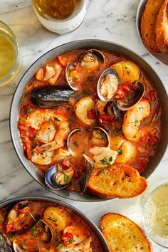 two pans filled with seafood and bread on top of a marble counter next to wine glasses