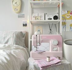 a pink sewing machine sitting on top of a bed next to a white shelf filled with items