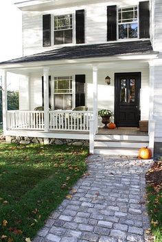 a white house with black shutters and a brick walkway leading to the front door