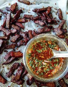 a glass bowl filled with sauce next to sliced meat on top of a white cloth