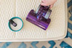 someone is using a purple vacuum to clean the mattress