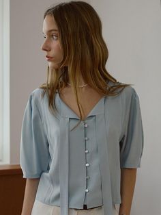 The Bailey Tie Blouse features a graceful design with its understated tie detail at the neckline, lending a soft touch to its structured look. This blouse is crafted with a flowing fabric that elegantly drapes over the body, highlighted by subtle front pleating that adds texture and depth. The blouse's muted tone and button-down front provide a versatile backdrop for both professional and casual outfits. - The blouse's light fabric is perfect for comfortable all-day wear, offering a blend of breathability and softness.- Its unique neckline tie adds a fashionable twist, allowing for customization in styling, whether tied neatly or left loose for a more casual look.- The button details are both functional and aesthetically pleasing, contributing to the blouse's refined appearance.- This Elegant Solid Color Blouse For Summer, Elegant Solid Blouse For Summer, Semi-formal Solid V-neck Top, Feminine Solid Color V-neck Blouse, Solid Feminine V-neck Blouse, Elegant V-neck Top, Solid Color Chic Blouse For Daywear, Chic Solid Color Blouse For Daywear, Elegant Solid Color Padded Blouse