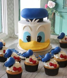 cupcakes with frosting and decorations are arranged in front of a donald the duck cake