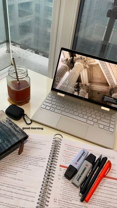 an open laptop computer sitting on top of a desk next to a notebook and pen