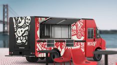 a red and black food truck parked in front of a table with chairs on it