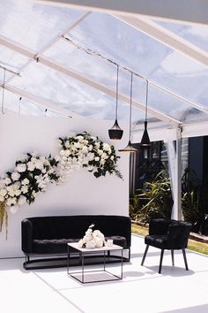 a living room filled with black furniture and white flowers hanging from the ceiling above it