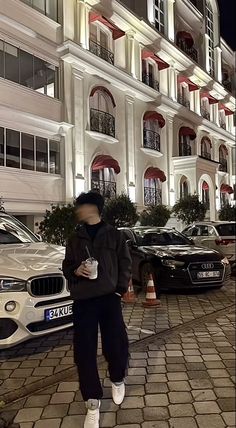 a man standing in front of a building with cars parked on the side of it