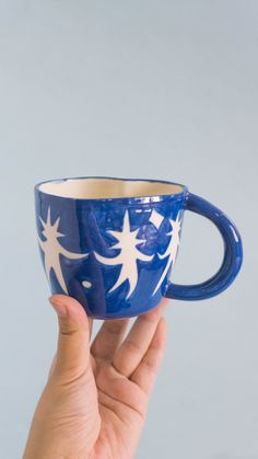 a hand holding a blue and white coffee cup with stars painted on the outside of it