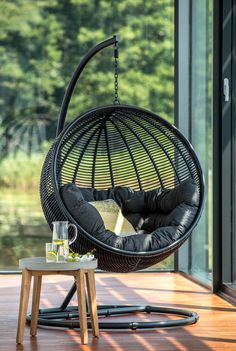 a black hanging chair on a wooden floor next to a table with a drink in it