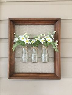 three mason jars with daisies are hung on the wall