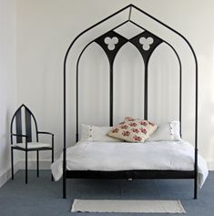 a white bed with black iron frame and headboard is in a room next to a chair