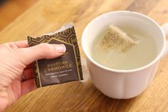 a hand holding a small bar of egyptian chamomile next to a cup of tea