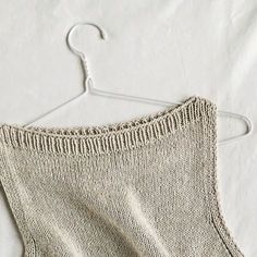 a knitted sweater hanging on a hanger with white sheets in the back ground