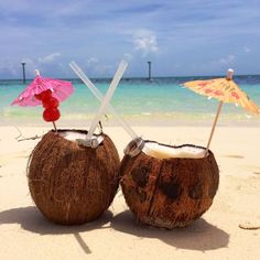 two coconuts on the beach with umbrellas sticking out of them