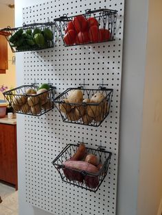 three baskets are hanging on the wall with food in them and one is filled with vegetables