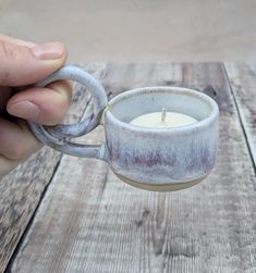 a person holding a small cup with a candle in it on top of a wooden table