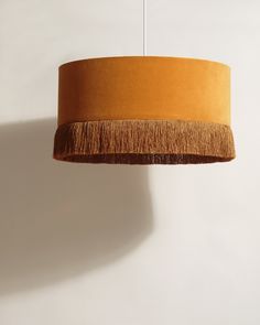 an orange lamp shade hanging from a white wall with a brown fringe on the bottom