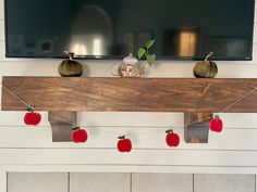 a flat screen tv mounted on top of a wooden mantle with apples hanging from it