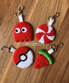 three red and white crocheted keychains with faces on them sitting on a wooden surface