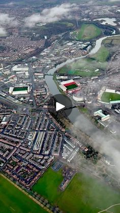 an aerial view of a large city with lots of green fields and clouds in the sky