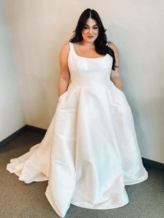 a woman in a white dress standing next to a wall with her hands on her hips