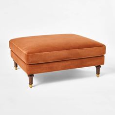 an orange footstool with wooden legs on a white background in front of a plain backdrop